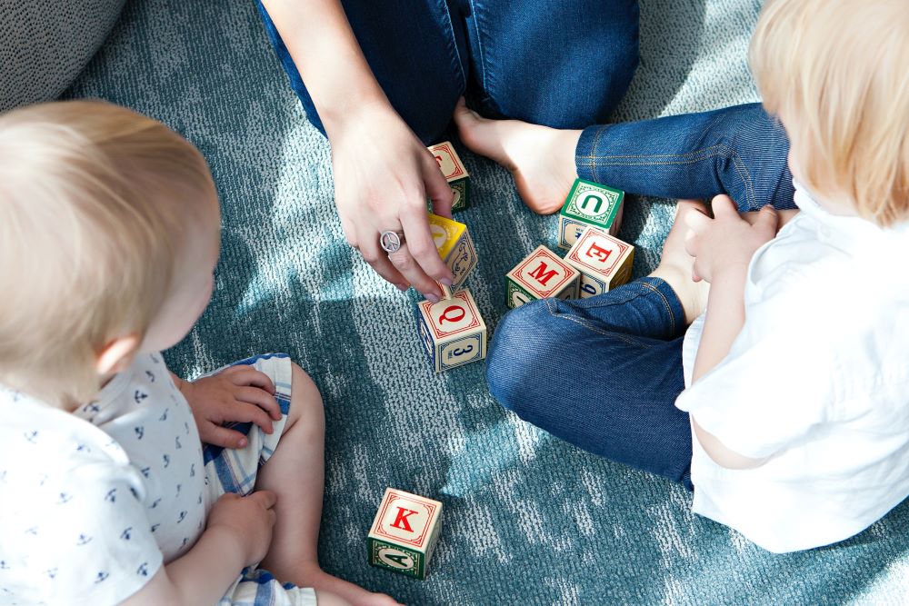 Young woman teaching toddlers letters with blocks. 